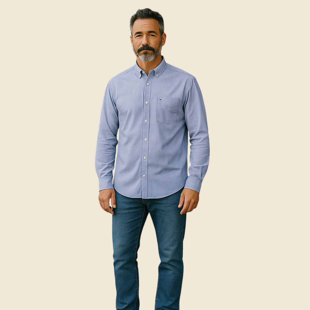 Man wearing a light blue button-up shirt and dark jeans on a beige background