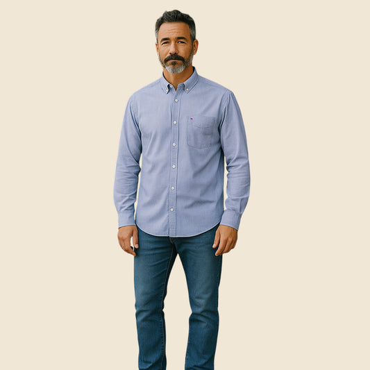 Man wearing a light blue button-up shirt and dark jeans on a beige background