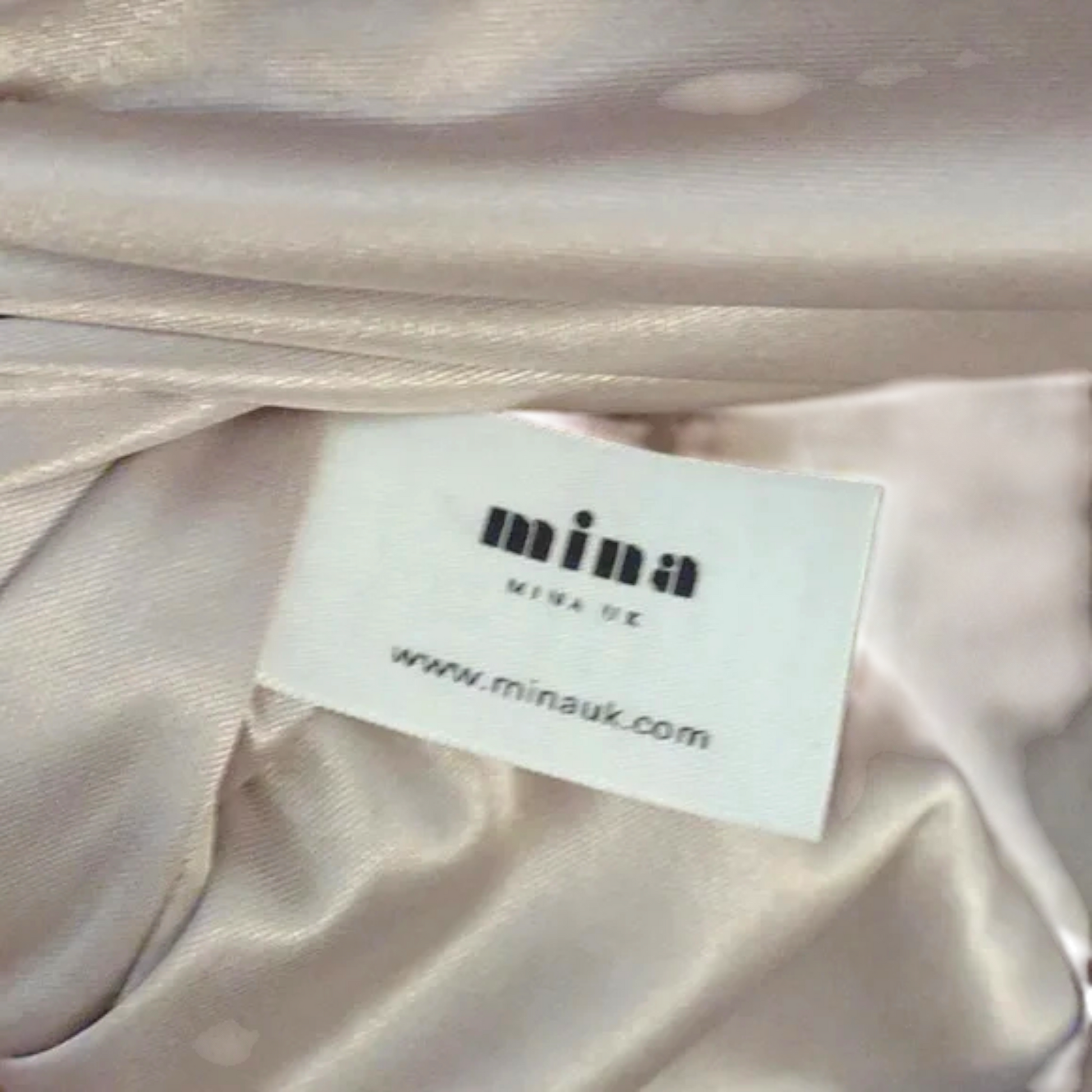 Close-up of a label on satin fabric with 'mina' branding.