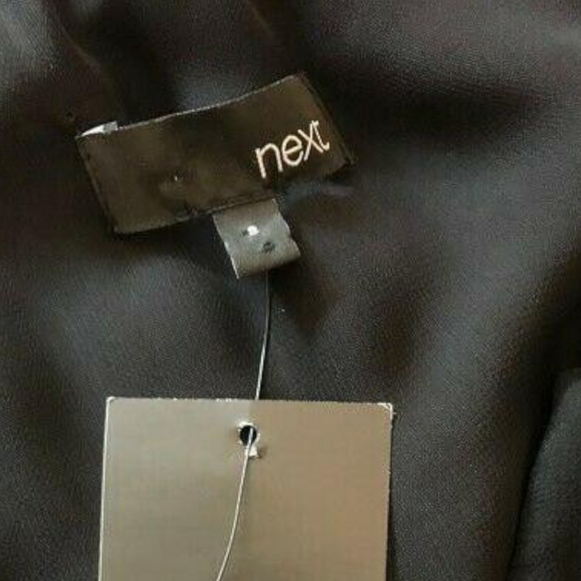Clothing tag with 'next' brand on a dark fabric background
