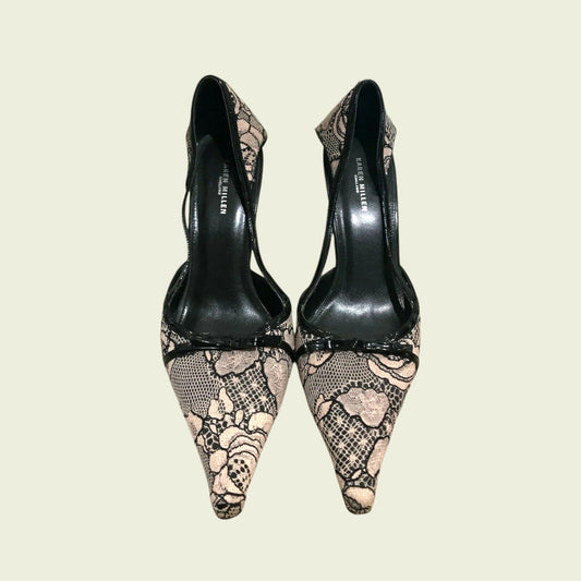 Pair of black high-heeled shoes with lace detailing on a beige background