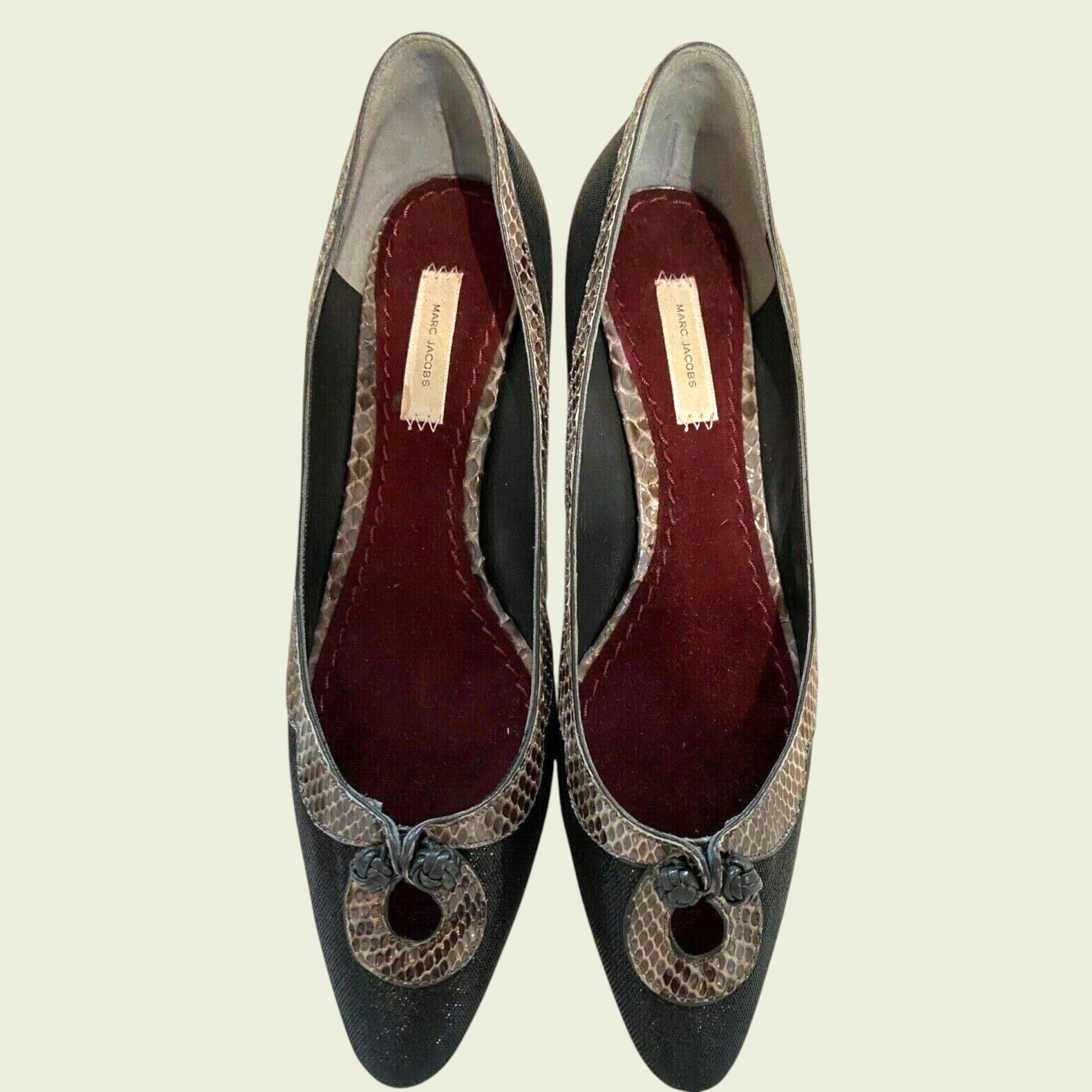 Pair of black high-heeled shoes with snake skin pattern on a beige background