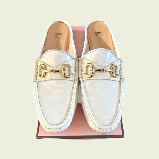 White loafers with gold accents on a pink and brown shoe box against a light beige background