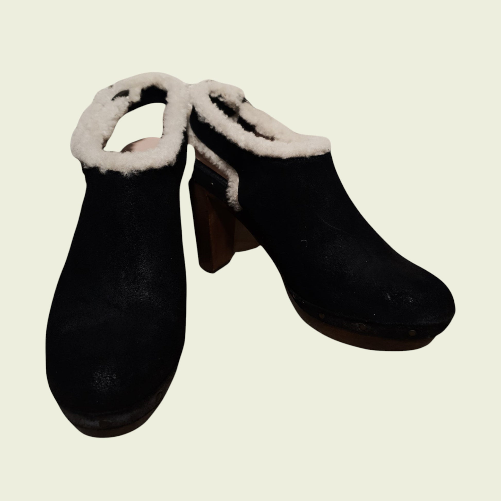 Pair of black clogs with white fur trim on a beige background