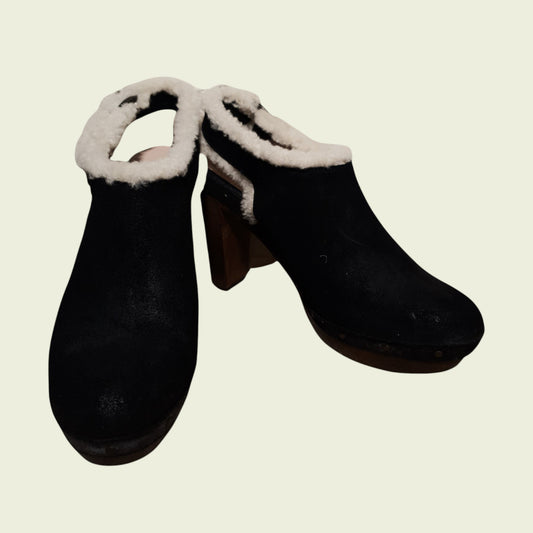 Pair of black clogs with white fur trim on a beige background