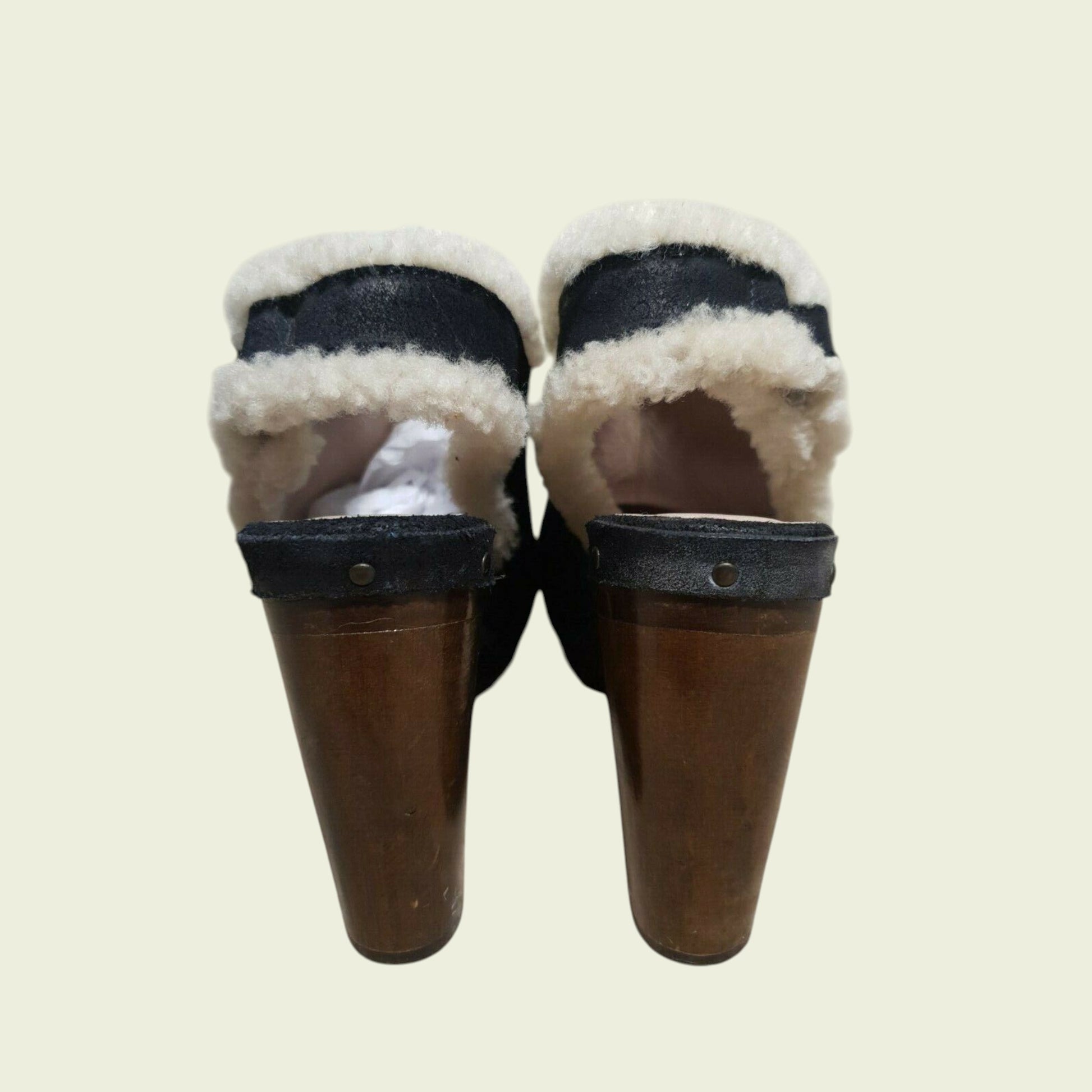 Pair of black mules with white fur lining on a beige background