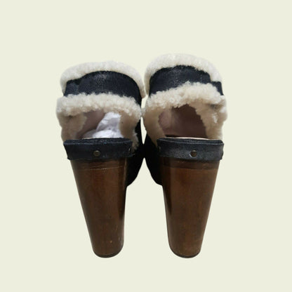 Pair of black mules with white fur lining on a beige background