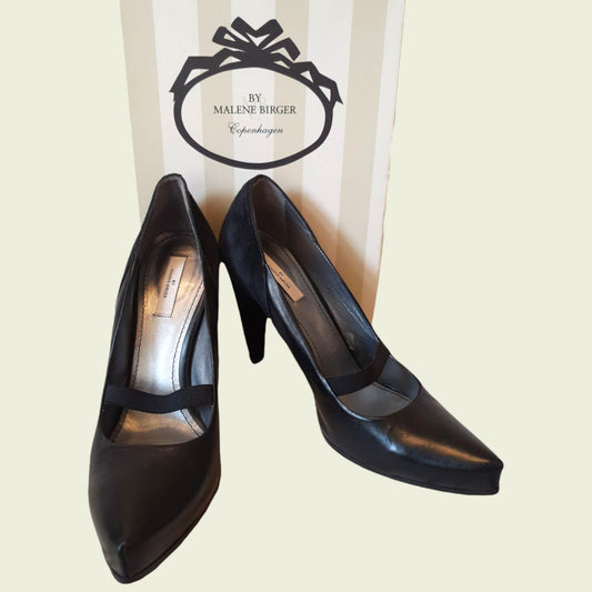 Black high-heeled shoes with a brand label in the background