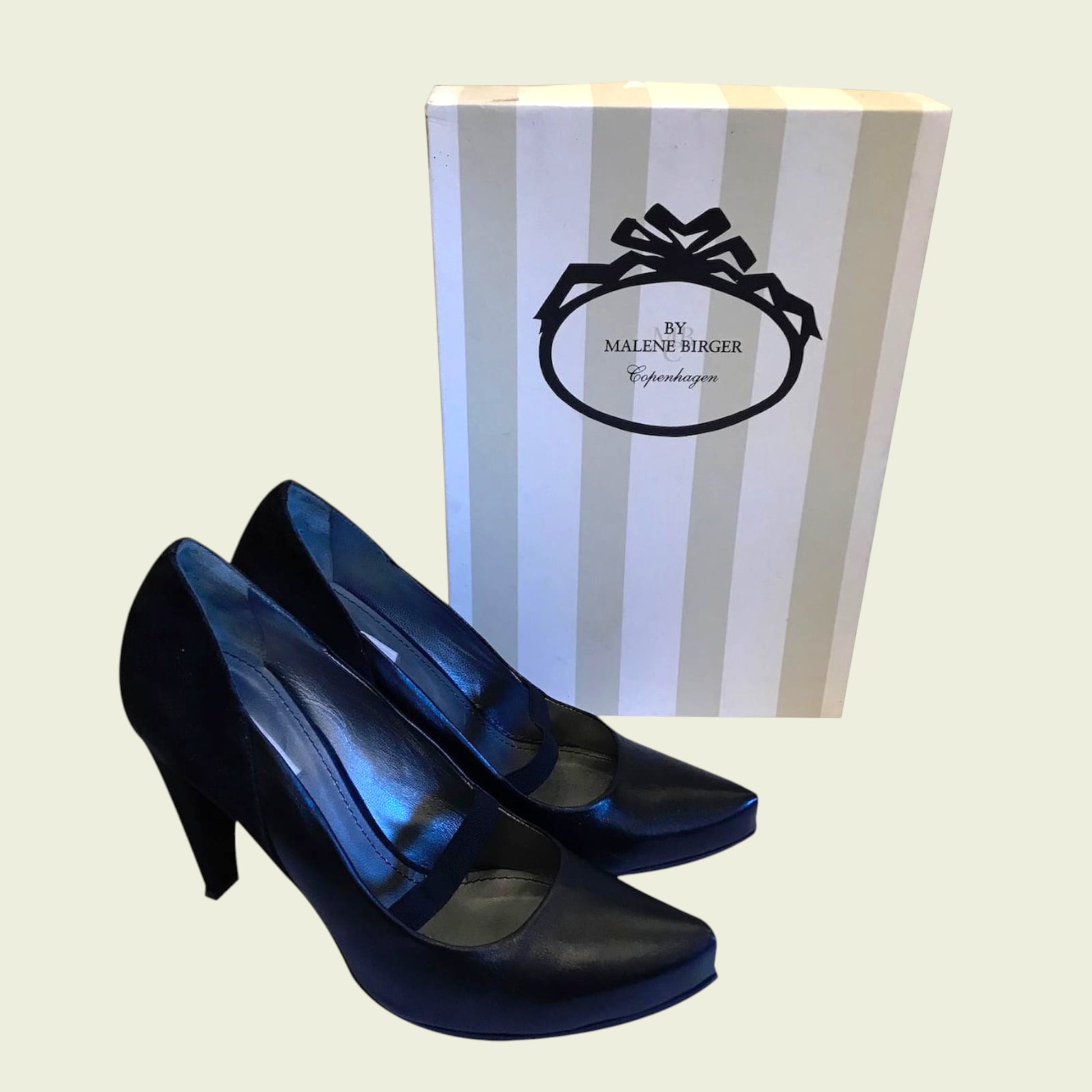 Pair of black high-heeled shoes with a striped box in the background