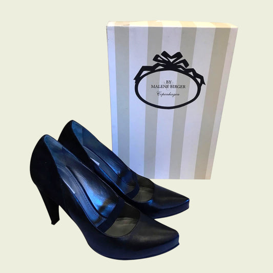 Pair of black high-heeled shoes with a striped box in the background