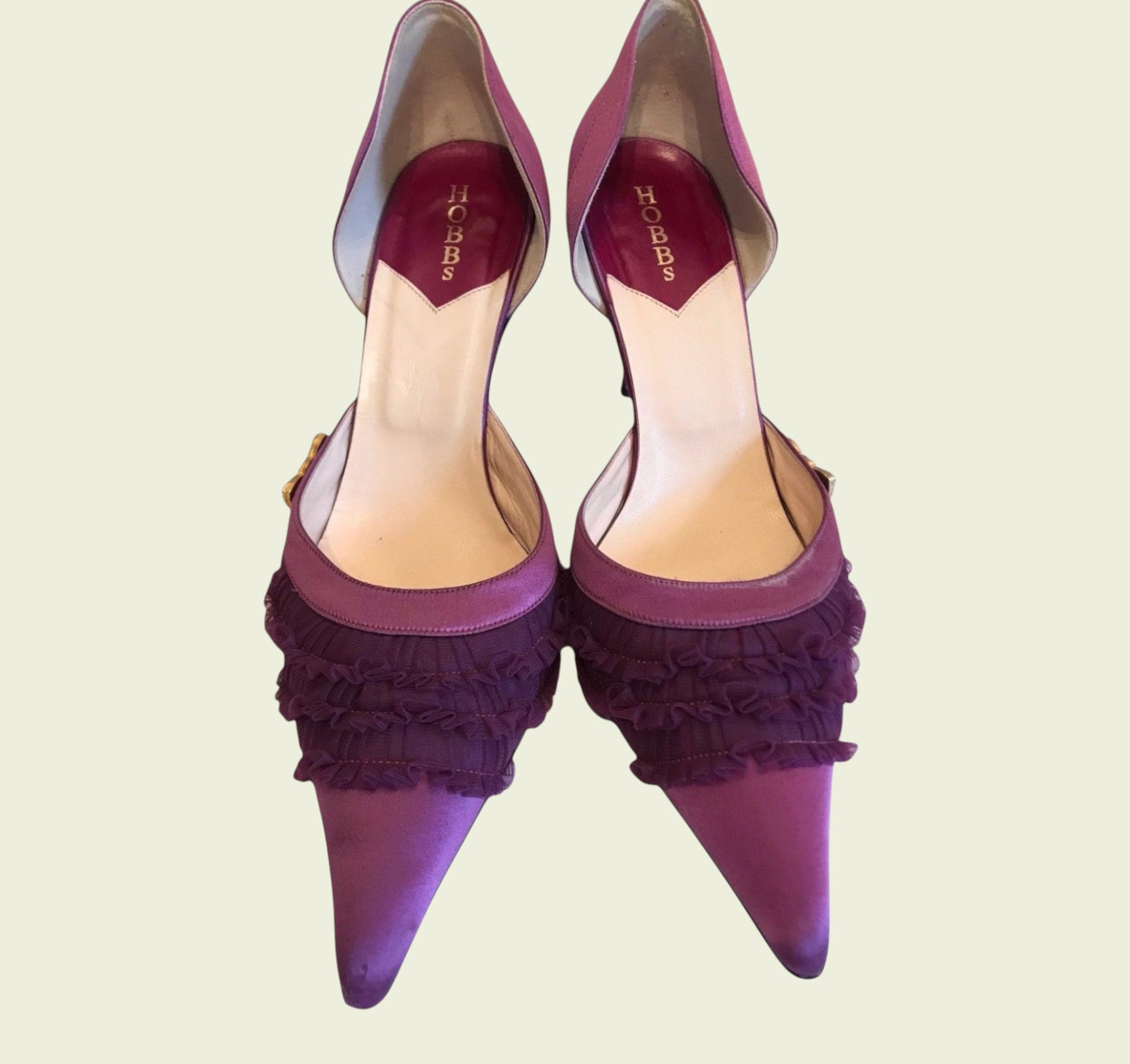 Purple high-heeled shoes with ruffled detailing on a light beige background