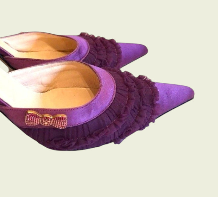 Purple high-heeled shoes with ruffles and a bow on a light background