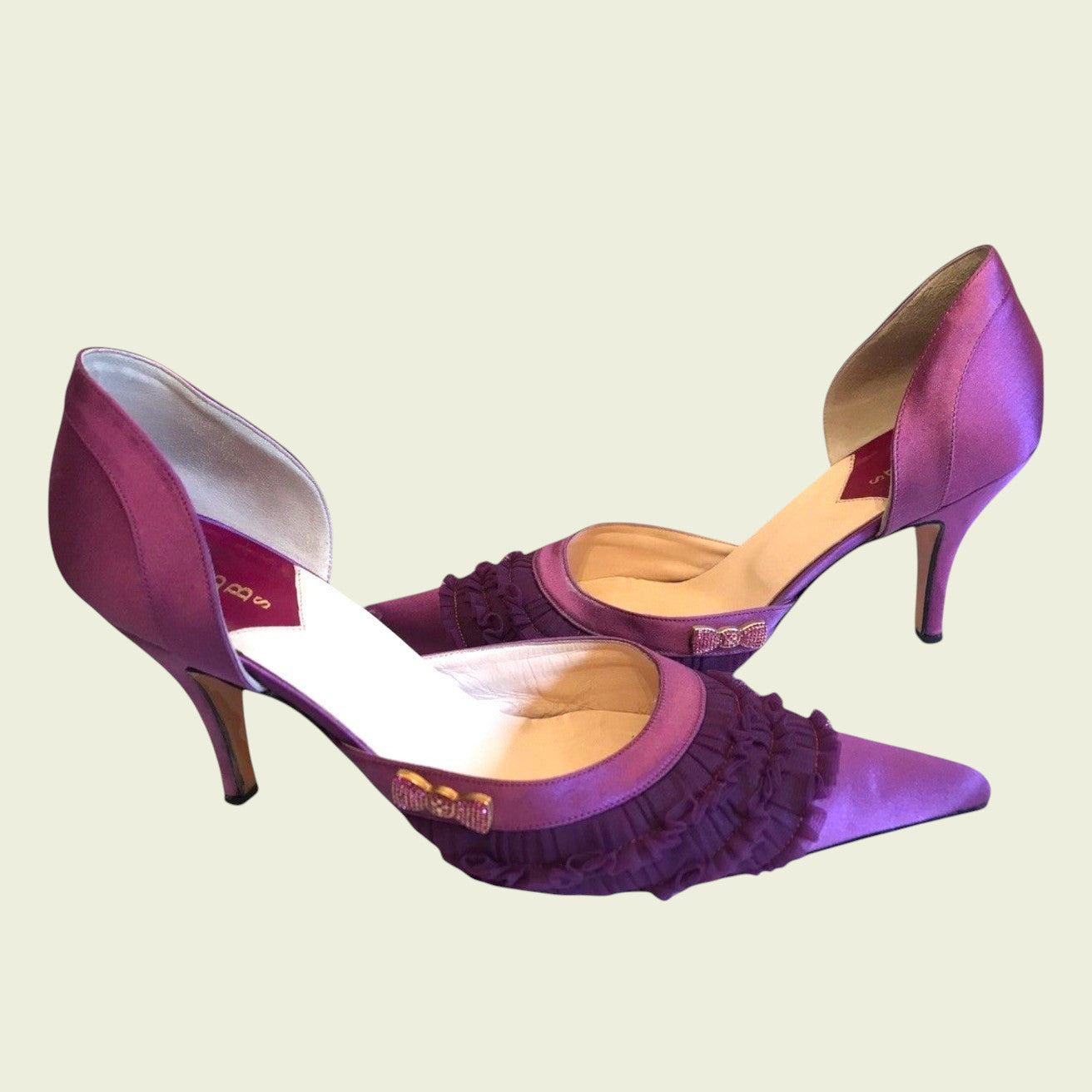 Purple high-heeled shoes with ruffled details on a light beige background