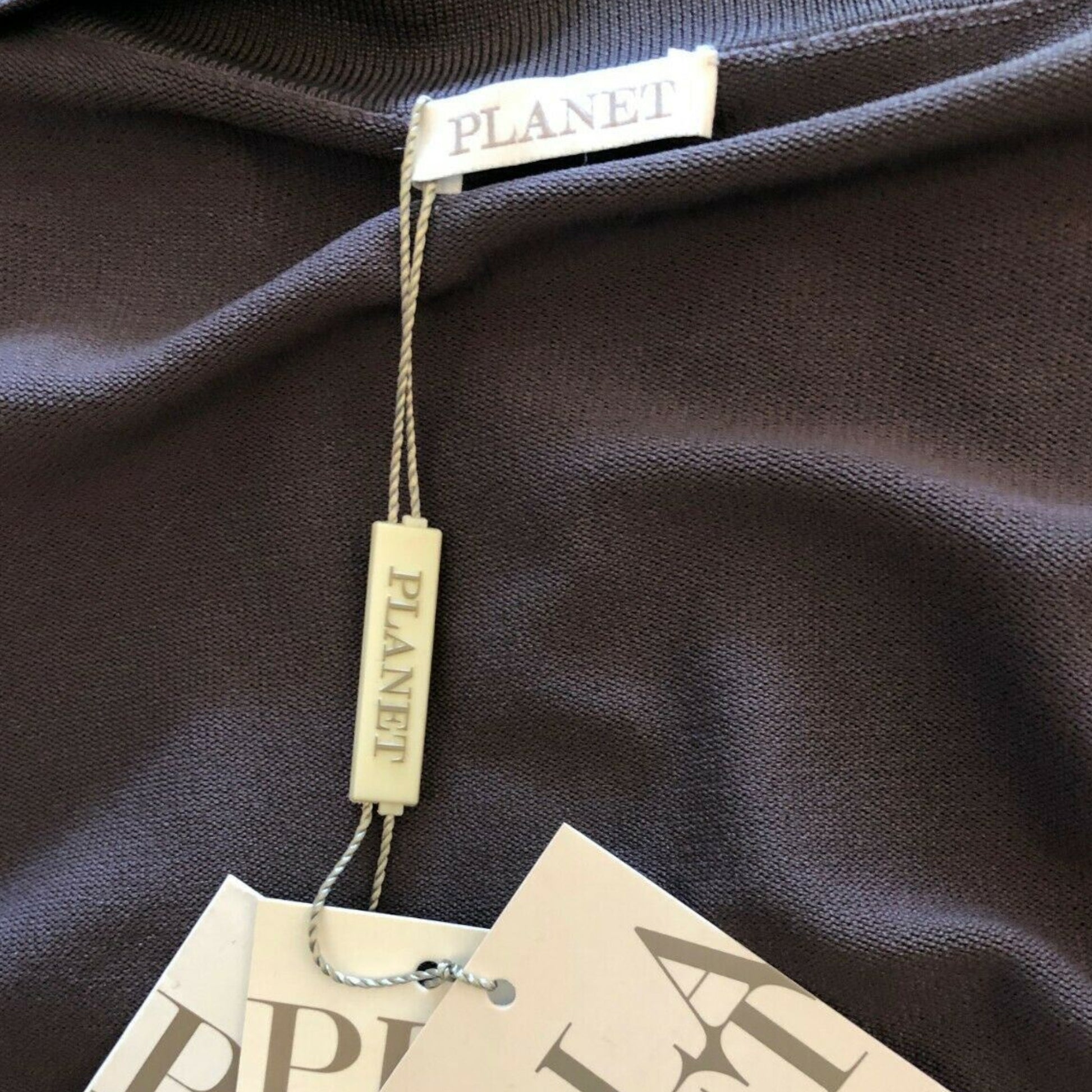 Close-up of a brown garment with 'PLANET' brand tags on a dark fabric background.
