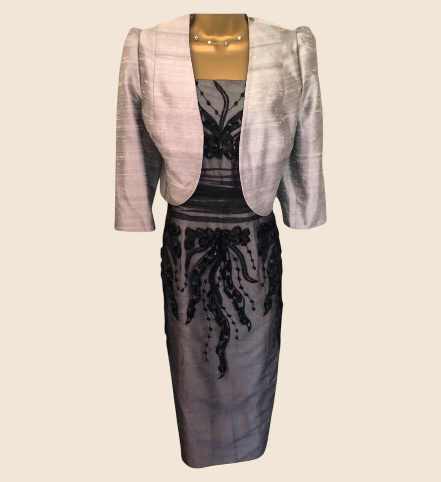Gray dress with lace detailing and a matching bollero on a mannequin against a beige background