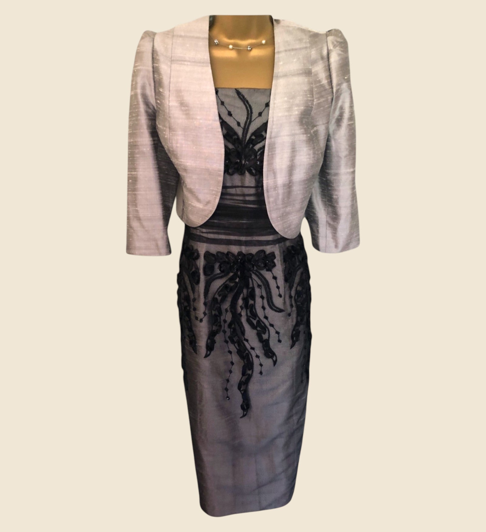 Gray dress with lace detailing and a matching bollero on a mannequin against a beige background