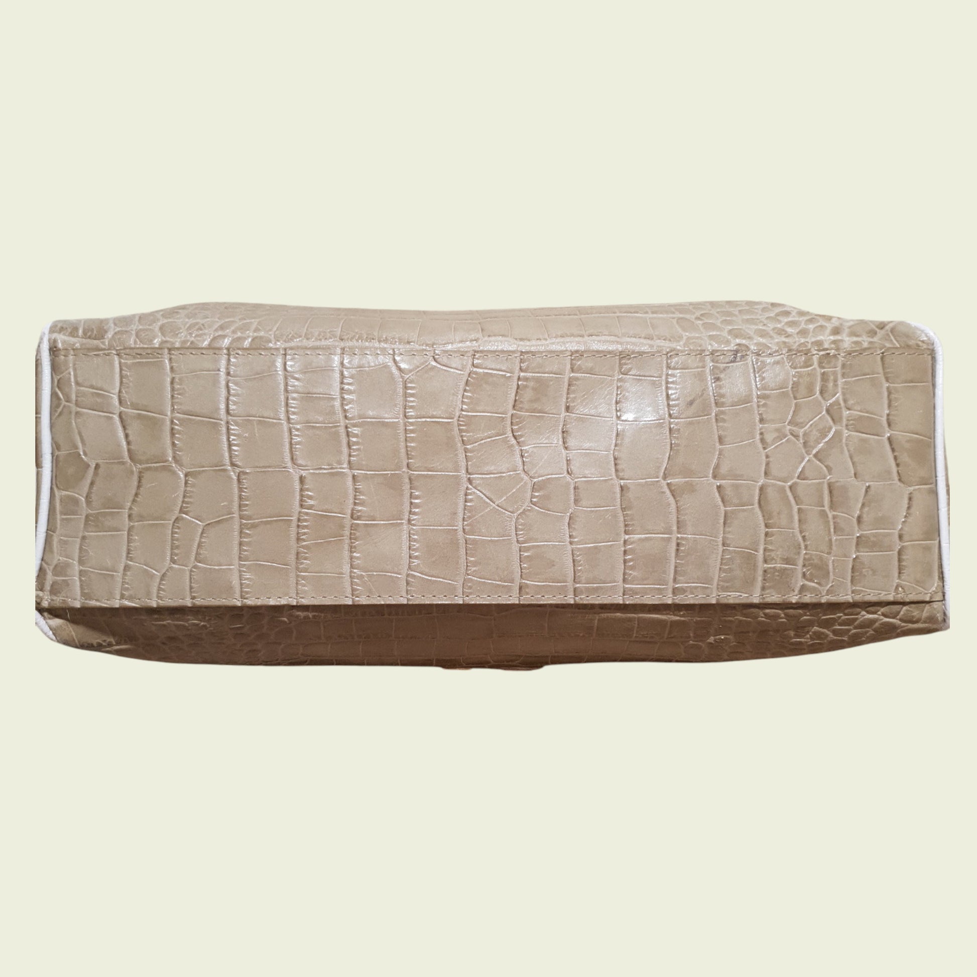 Bottom of bag with crocodile texture on a beige background