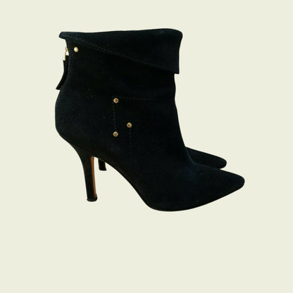 Black high-heeled boots with gold buttons on a beige background