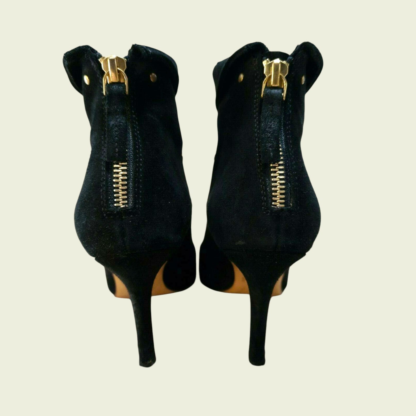 Black high-heeled shoes with gold zippers on a beige background