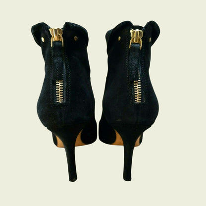Black high-heeled shoes with gold zippers on a beige background