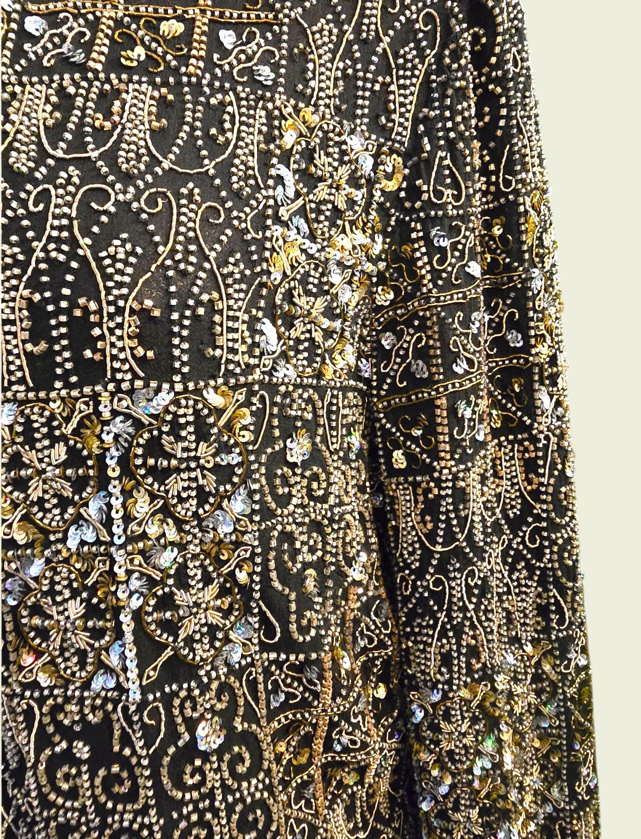 Close-up of a black fabric with gold and silver embroidery on a beige background
