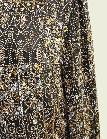 Close-up of a black fabric with gold and silver embroidery on a beige background