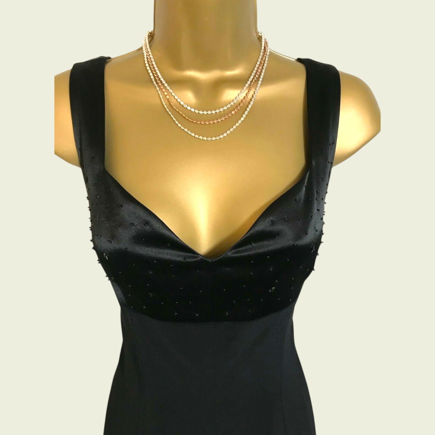 Black dress on a mannequin with pearl necklaces against a beige background