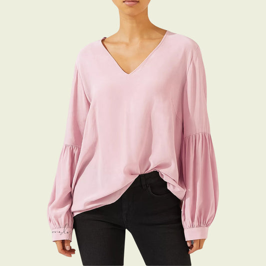 Pink blouse with long sleeves worn by a person on a light green background