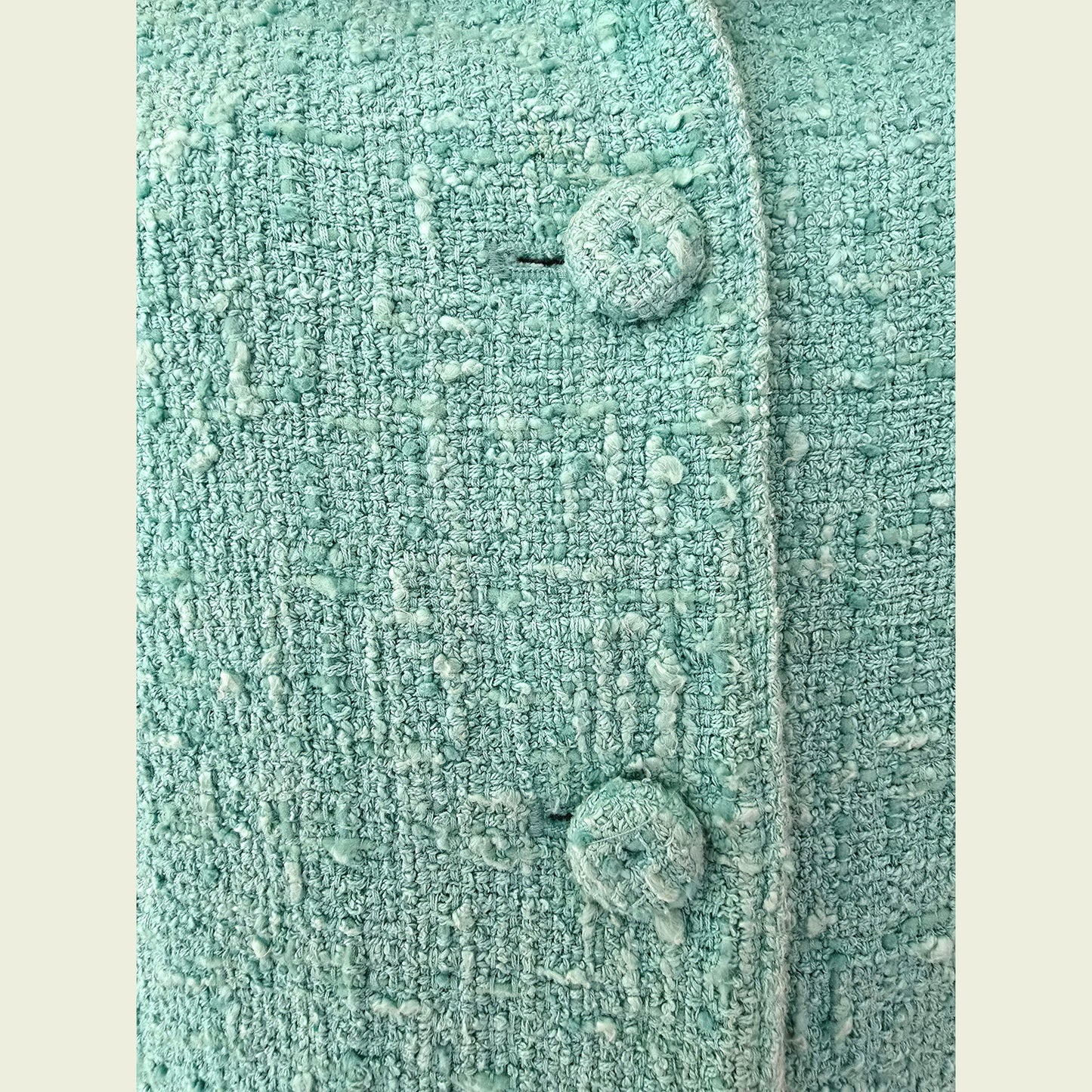 Close-up of a textured turquoise fabric with buttons on a beige background