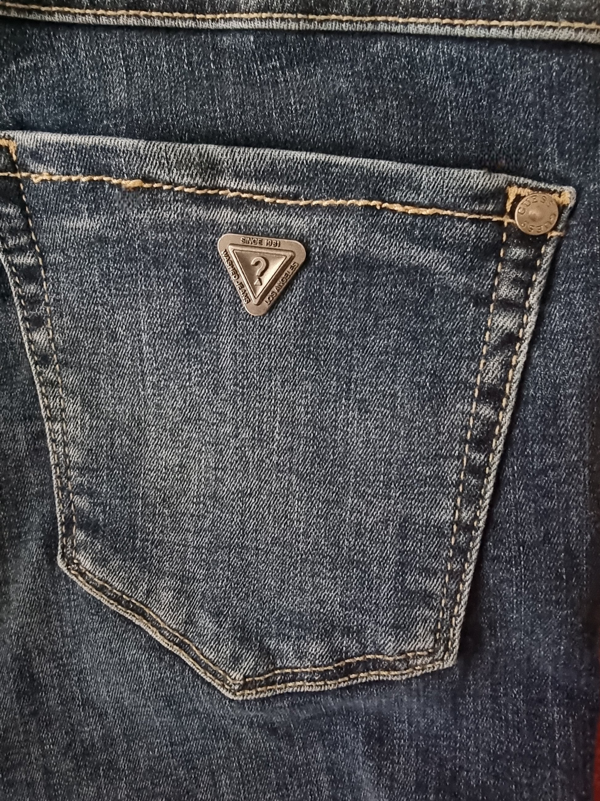 Close-up of a blue denim pocket with a brand logo on a dark background