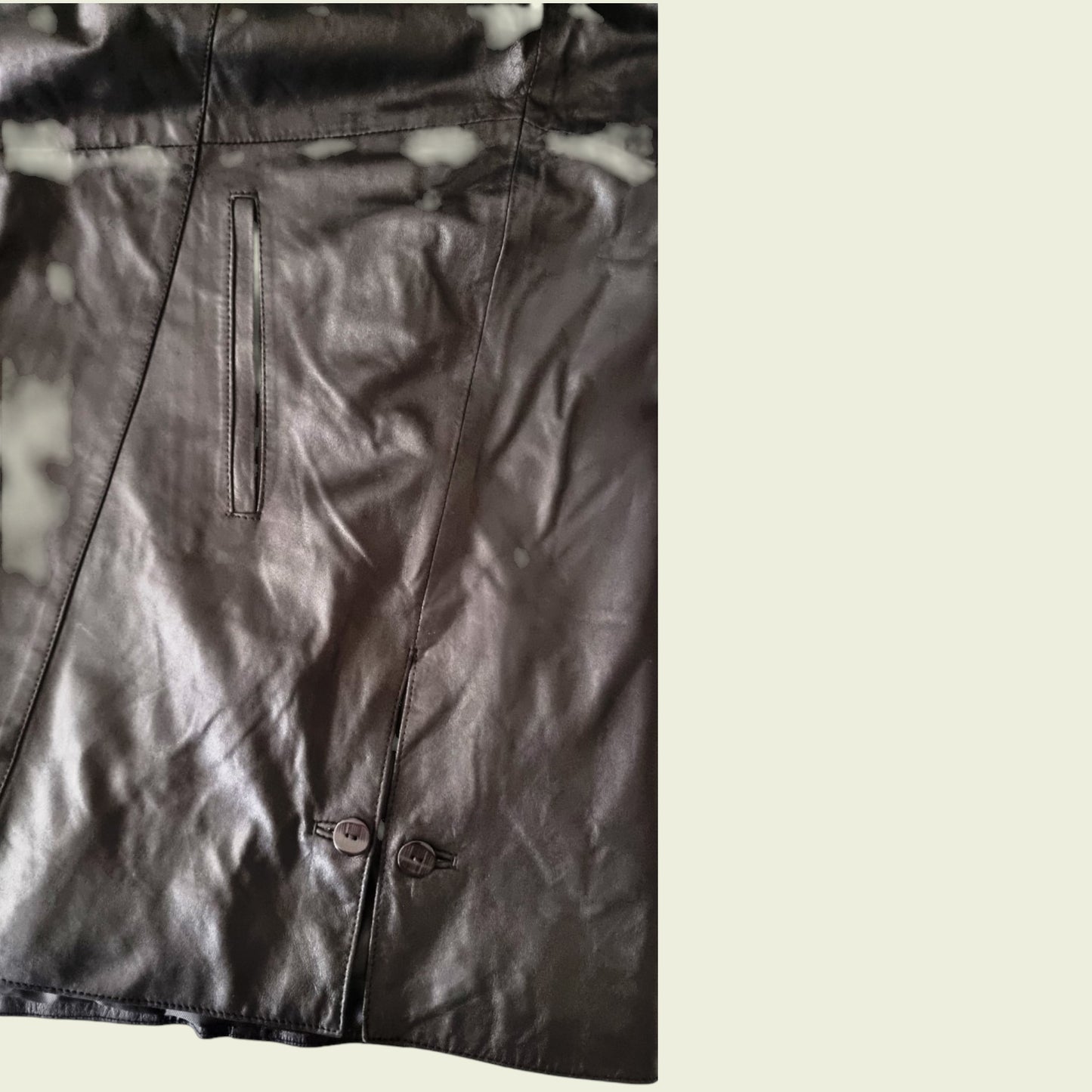 Close-up of a black leather jacket with buttons on a light background