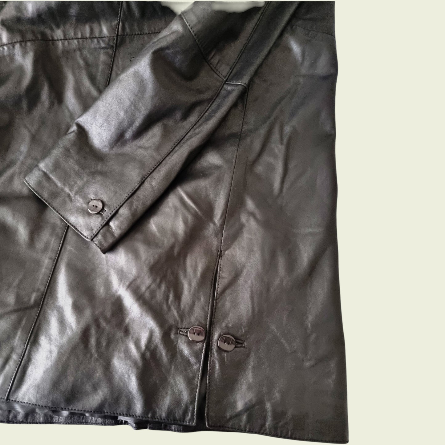 Close-up of a black leather jacket with buttons on a light background