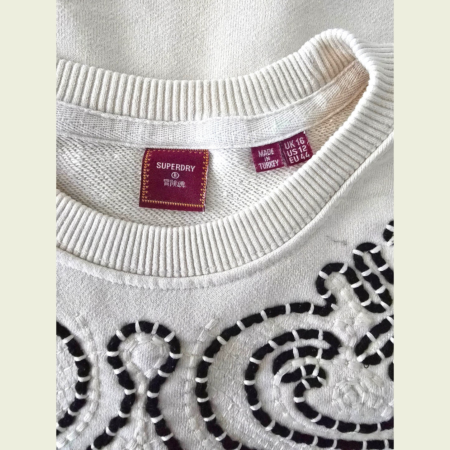 Close-up of a beige sweater with brown patterns and Superdry label.