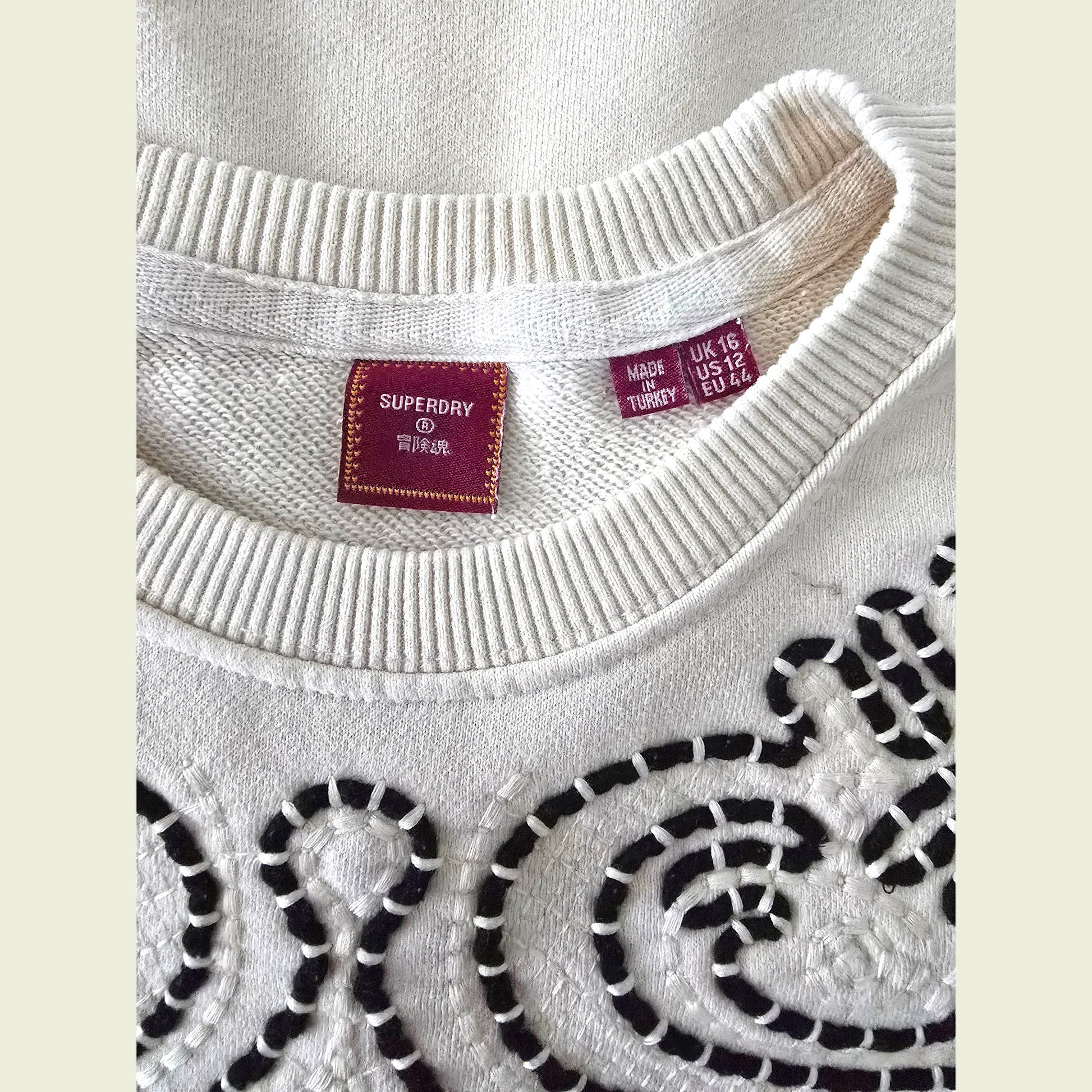 Close-up of a beige sweater with brown patterns and Superdry label.