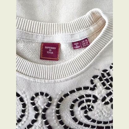 Close-up of a beige sweater with brown patterns and Superdry label.