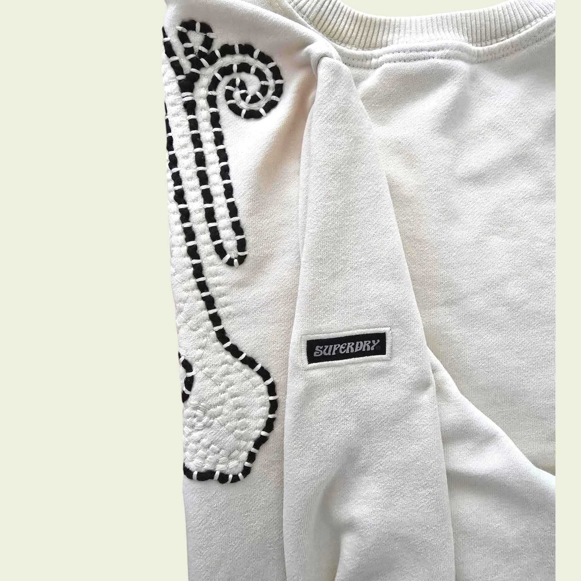 Beige sweatshirt with brown pattern and Superdry logo on a light beige background