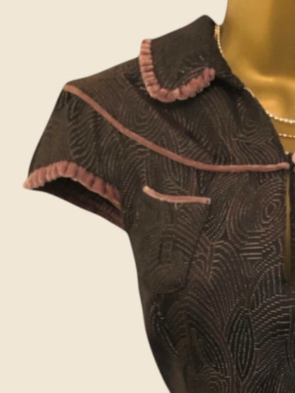 Close-up of a dark fabric garment with intricate patterns and pink trim on a beige background