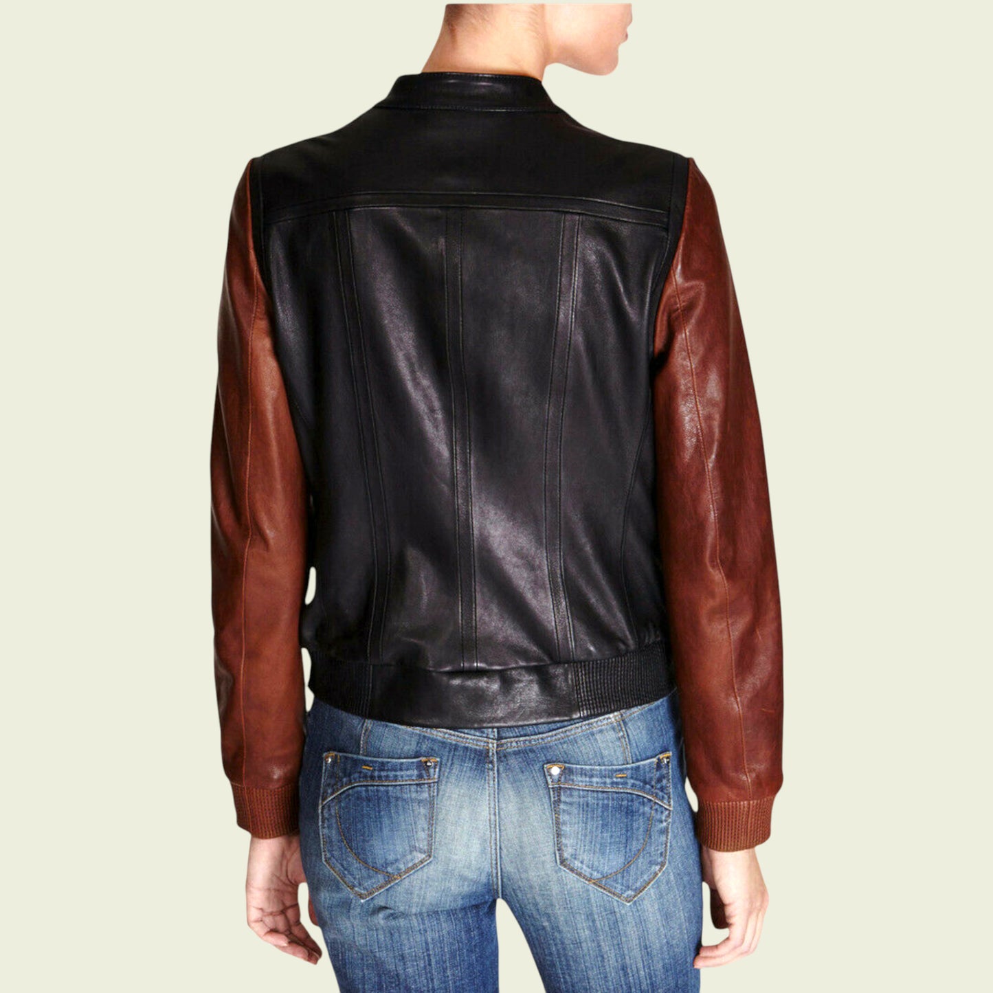 Person wearing a black and brown leather jacket with blue jeans on a beige background